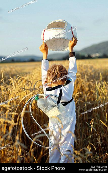 Boy wearing astronaut costume holding space helmet at field