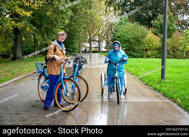 41 yo woman with the Down Syndrome sitting on a tricycle with her 37 yo friend on a bike outdoors, Tienen, Flanders, Belgium