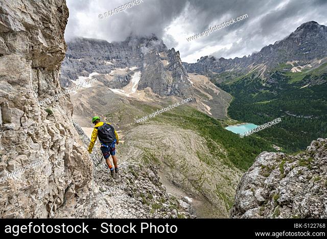Young man, mountaineer on a fixed rope route, Via Ferrata Vandelli, view of Lago di Sorapis, Sorapiss circuit, mountains with low clouds, Dolomites, Belluno