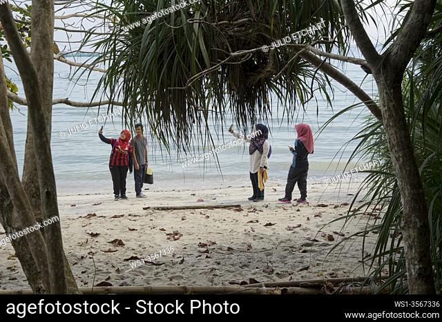 Local Malay visitors taking smartphone selfies at a each by the rainforest in the Taman Negara Pulau Pinang nature reserve national park in Penang, Malaysia