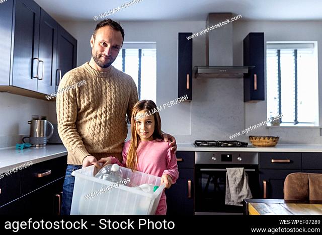 Smiling father with girl recycling plastic bottles in kitchen at home