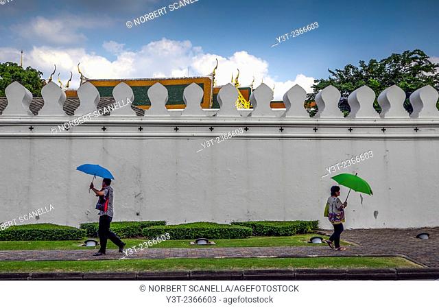 Asia. Thailand, Bangkok. People with umbrella walking front of king's palace wall