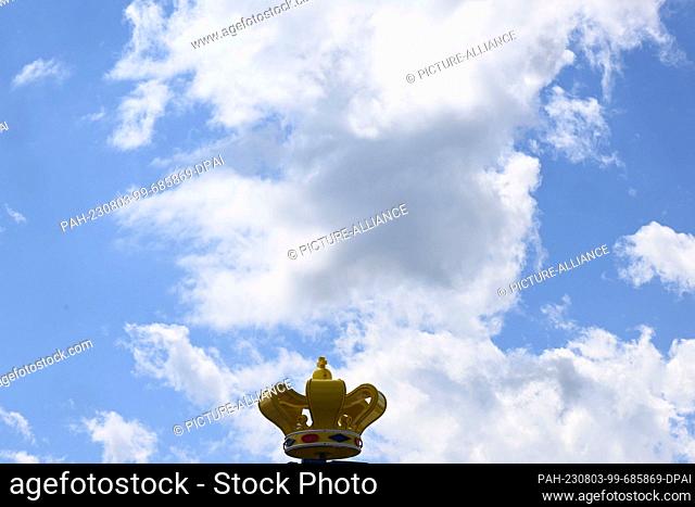 03 August 2023, Bavaria, Munich: White-blue clouds pass over the crown adorning the roof of the still unfinished Hofbräu tent during the Wiesn set-up on the...