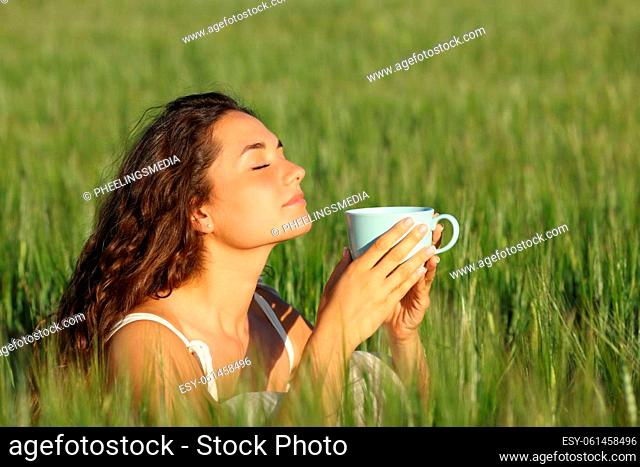 Woman relaxing smelling coffee from cup in a green wheat field