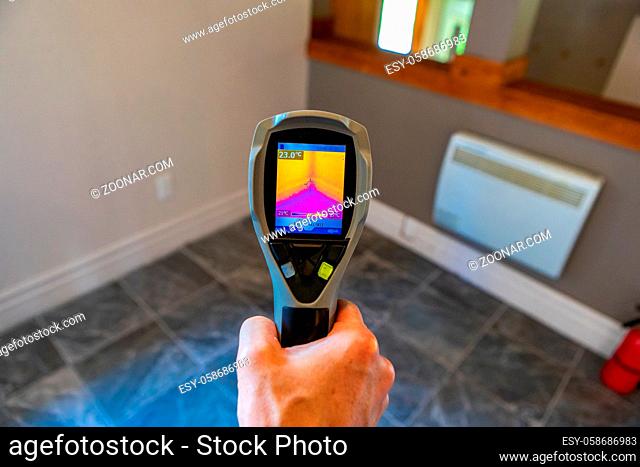 A close up view on the rear screen of an infrared thermal vision camera, pointing towards the corner of a room with cold tiled floor and warm insulated walls