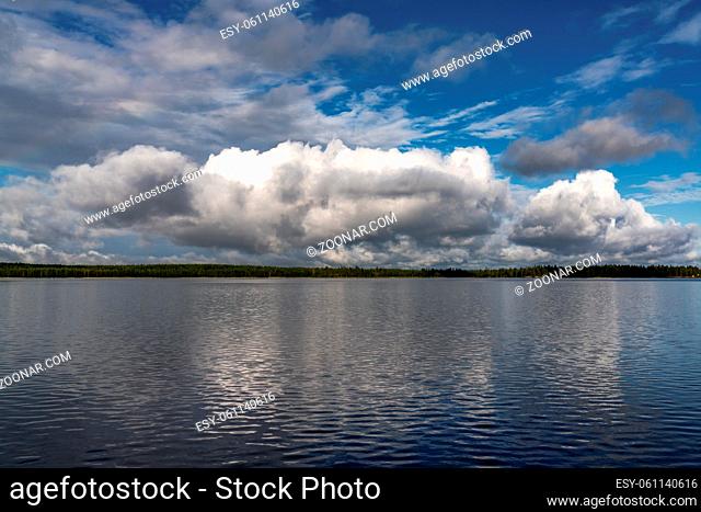 A calm and peaceful lake landscape in the wilderness with forest on the distant shore under an expressive blue sky with white clouds