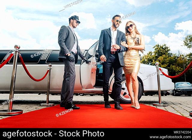 Couple arriving with limousine walking red carpet, a driver is opening the car door