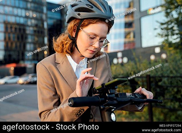 Young businesswoman using smart phone on electric push scooter