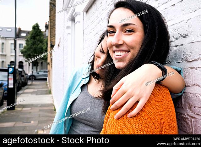 Smiling friends with arm around standing on footpath