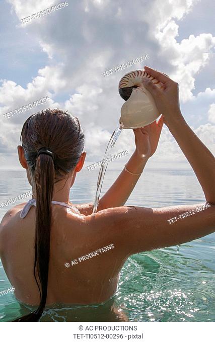 Woman in sea pouring water out of nautilus seashell