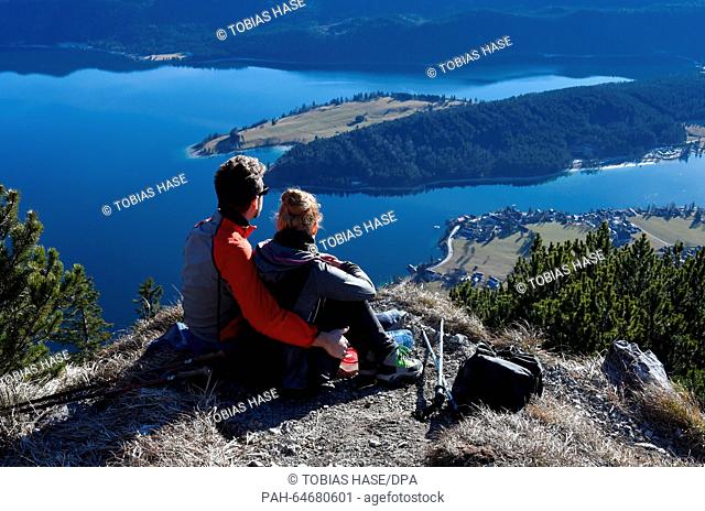 Two mountain hikers sit on the summit of the Herzogstand enjoying the warm sun near lake Walchensee, Germany, 26 December 2015