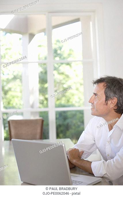 Man sitting at table with laptop looking out window