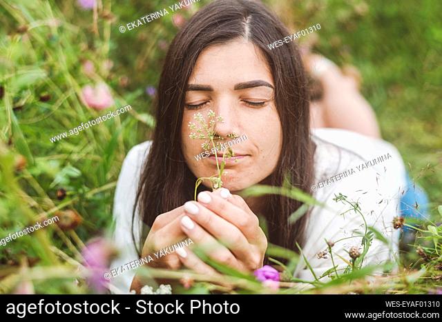 Close-up of mid adult woman with eyes closed smelling flowers while lying on land