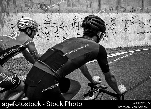 Cyclists ride by a wall with Tibetan inscription in Taipei, Taiwan on 07/06/2023 by Wiktor Dabkowski. - Taipei/Taipei/China