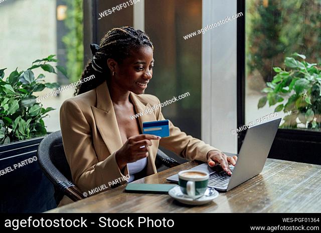 Young businesswoman paying with credit card through laptop at cafe