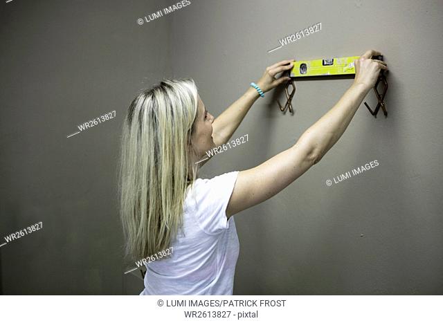Blonde woman measuring with water level to fix coat hooks