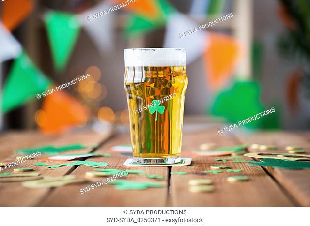glass of beer, shamrock and coins on wooden table
