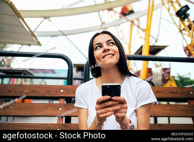 Young woman using smart phone while sitting on bench at amusement park