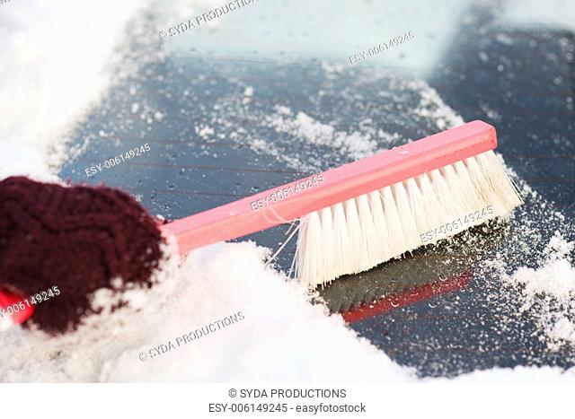 transportation, winter and vehicle concept - closeup woman cleaning snow from car back window with brush