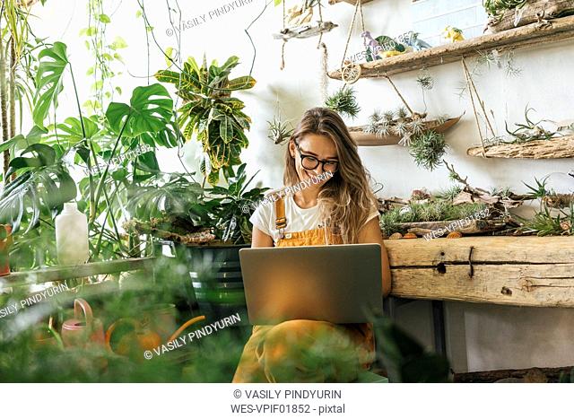 Happy young woman using laptop in a small gardening shop