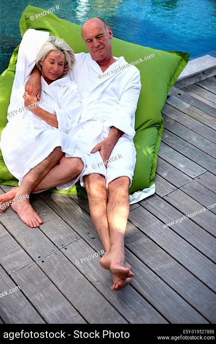 Senior couple in bathrobe sitting on the edge of a swimming pool