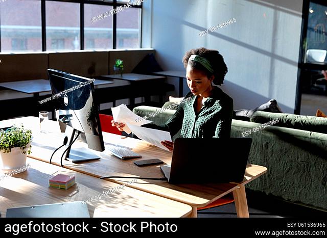 African american young businesswoman analyzing documents while sitting at computer desk in office