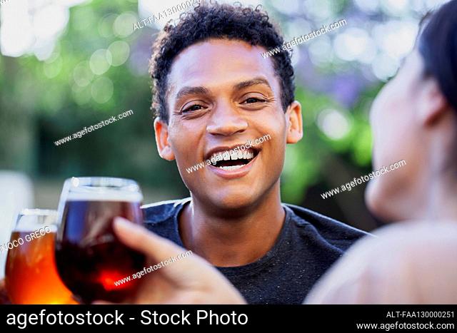 Latin American young man looking at the camera while having beer with friends