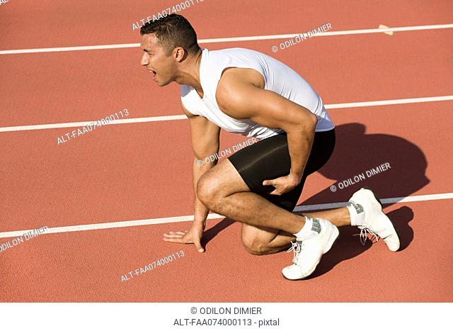 Injured runner kneeling on running track