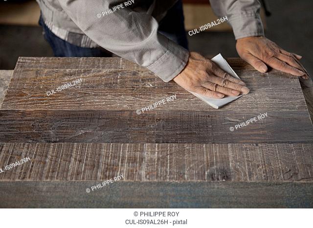 Carpenter smoothing surface of wood plank with sandpaper in factory, Jiangsu, China