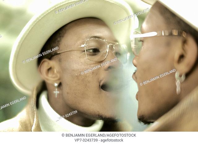 man breathing on mirror, looking at himself, self-perception, wearing Christian cross earring, faith, believe, in Munich, Germany