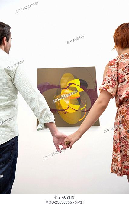 Married couple holding hands in front of painting in art gallery