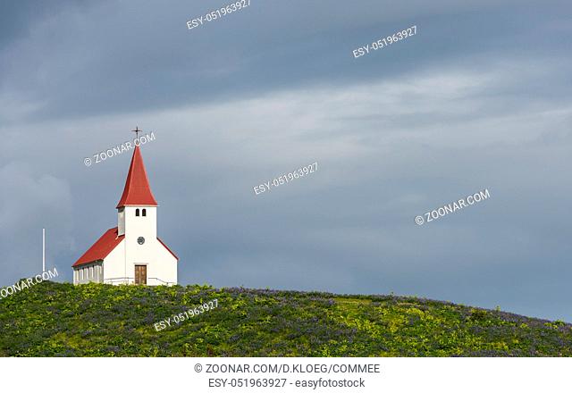 White church Vikurkirkja with red roof in Vik i Myrdal with dark clouds on Iceland