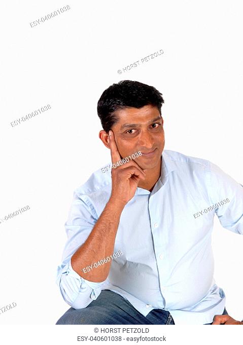 A closeup image of a good looking man in a blue shirt and jeans with.one hand on his face, isolated for white background