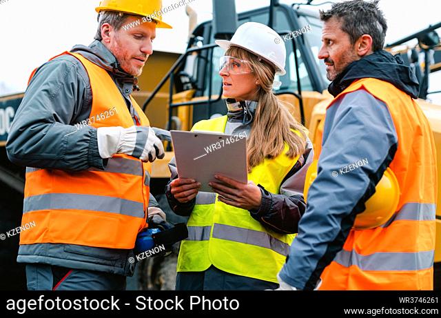 Three workers in a quarry discussing in front of heavy machinery looking at plan