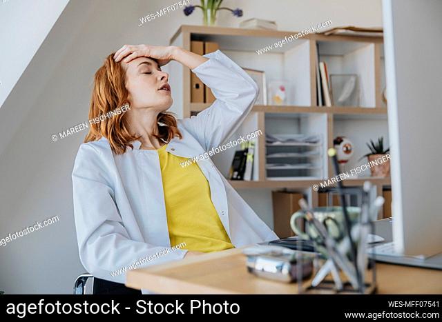 Frustrated female doctor sitting with head in hand at doctor's office