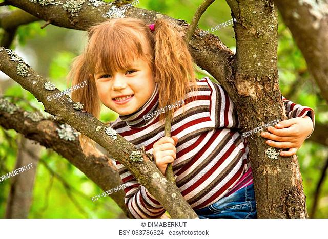 Lovely little girl posing sitting on a tree in the garden