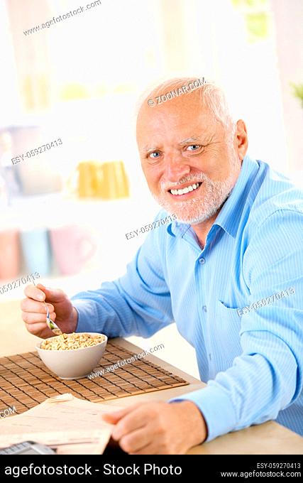 Portrait of healthy older man eating cereal for breakfast, looking at camera, smiling