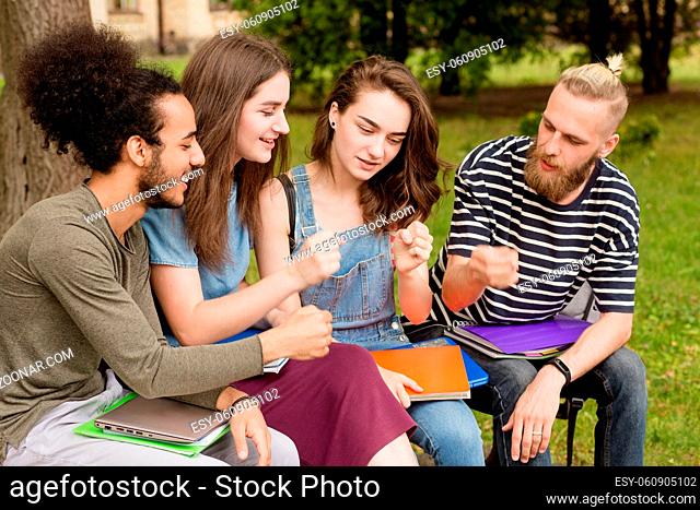 Multiethnic students sitting on bench playing games. Boys and girls sitting outdoors playing rock paper scissors