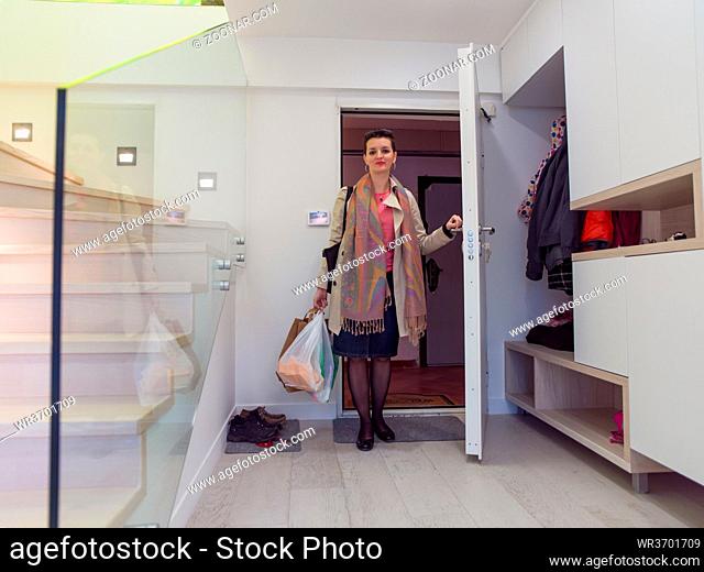 young employed woman returning home after work with bags of groceries in her hands standing on door in stylish interior of apartment entrance corridor