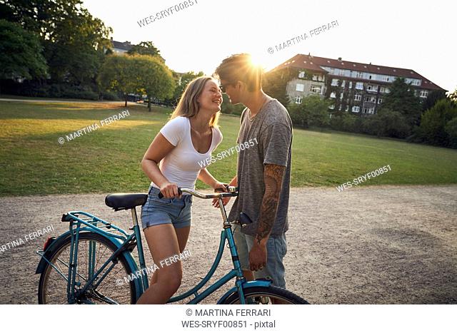Young woman with bicycle, kissing her boyfriend in park