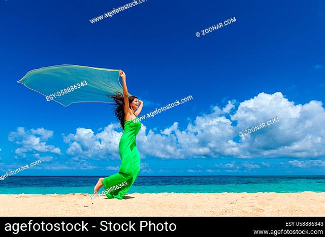 Young beautiful woman in dress run on beach holding fabric
