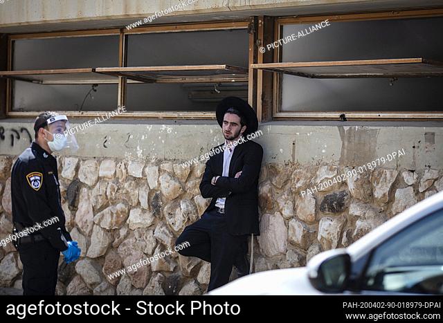 02 April 2020, Israel, Bnei Brak: An Israeli policeman speaks with an Orthodox Jewish young man, who insists on carrying on with his prayer at the Ponevezh...