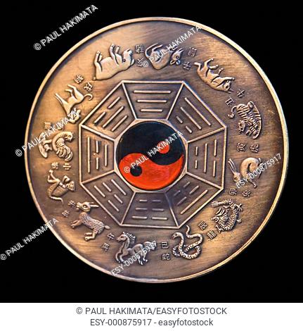 Lunar calendar depicted in a bronze medallion with a red and black ying yang in the middle, isolated on black