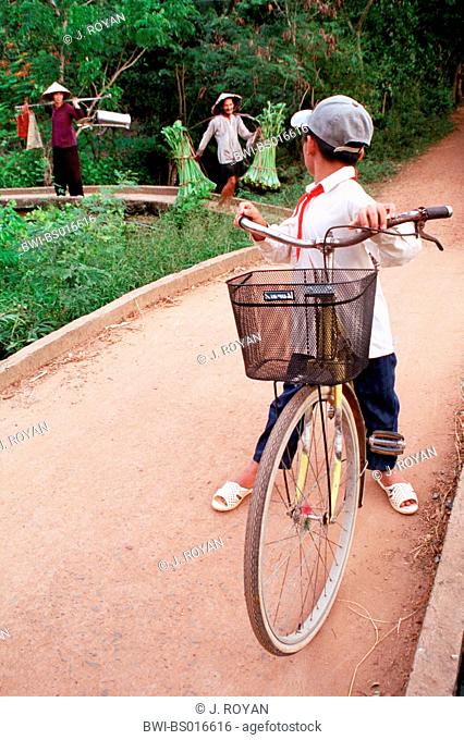 Vietnamese boy on bicycle, with two women in background, Vietnam
