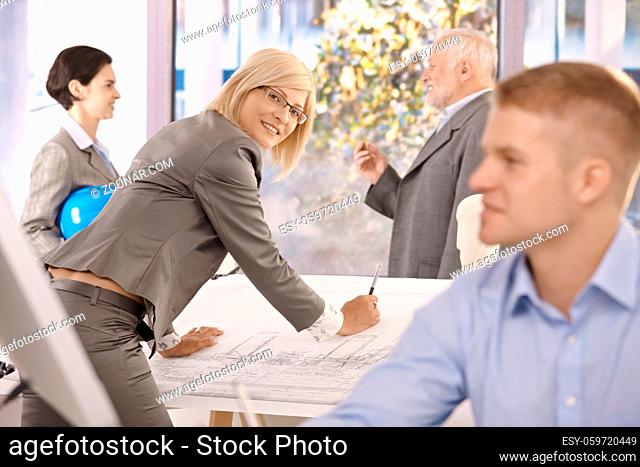 Architects working in office, female designer smiling at camera working on plan