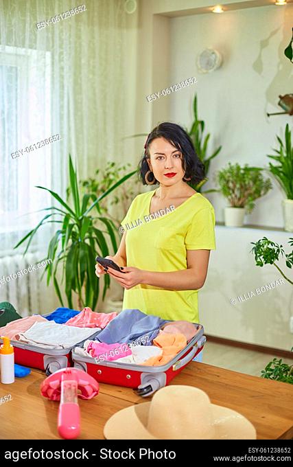 Travel woman packing suitcase, check things on the smartphone, getting ready for summer vacation trip preparing luggage for holidays