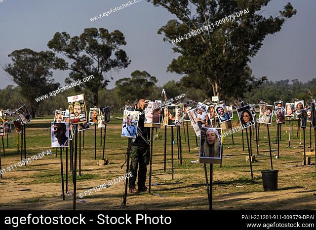 01 December 2023, Israel, Re'im: An Israeli soldier stands between the images of the killed Israelis at the site of the Re'im music festival massacre