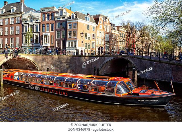 Stadtrundfahrt in einem Boot auf einer Gracht in Amsterdam, Niederlande im Frühling. Sightseeing boat on a canal in Amsterdam, Netherlands in spring