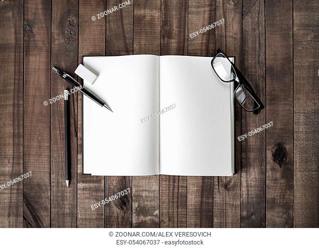 Photo of opened book with blank white pages and stationery on wood table background. Flat lay