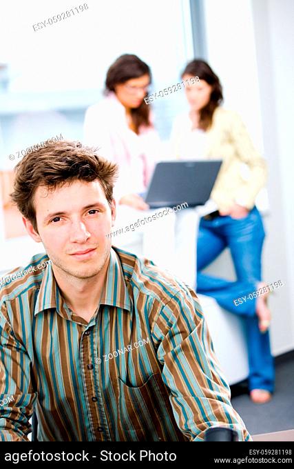 Young happy businessman looking at camera, smiling while business team working in background